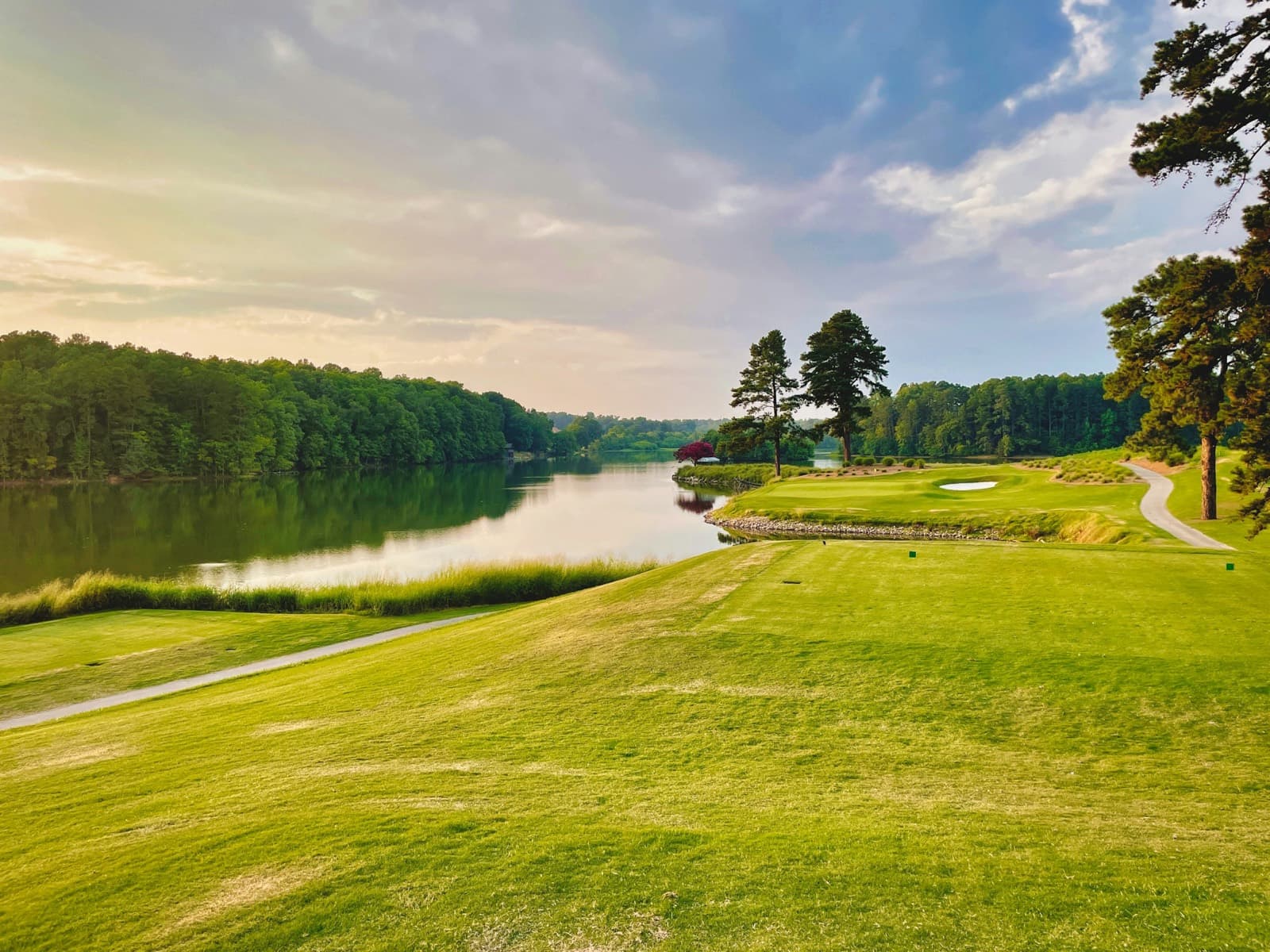 A fairway running along a lake lined with pines at sunset